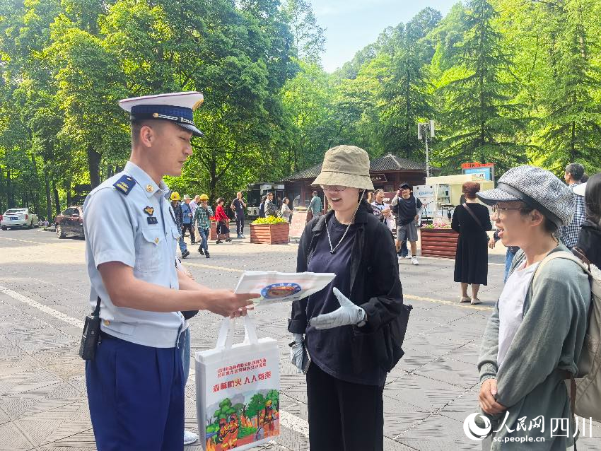 5月1日，青城山門口，消防員裴樂向游客發(fā)放防火宣傳單，普及森林防火常識。程雪力攝